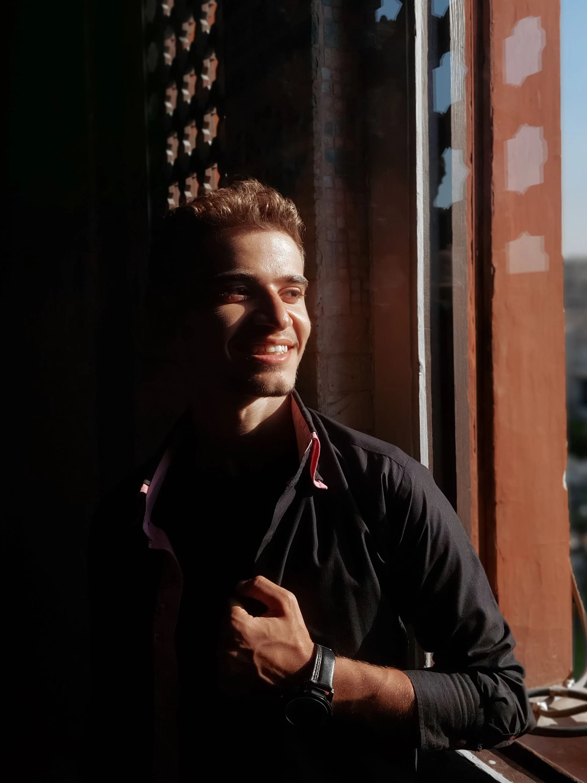 An adult smiling beside a naturally lit window