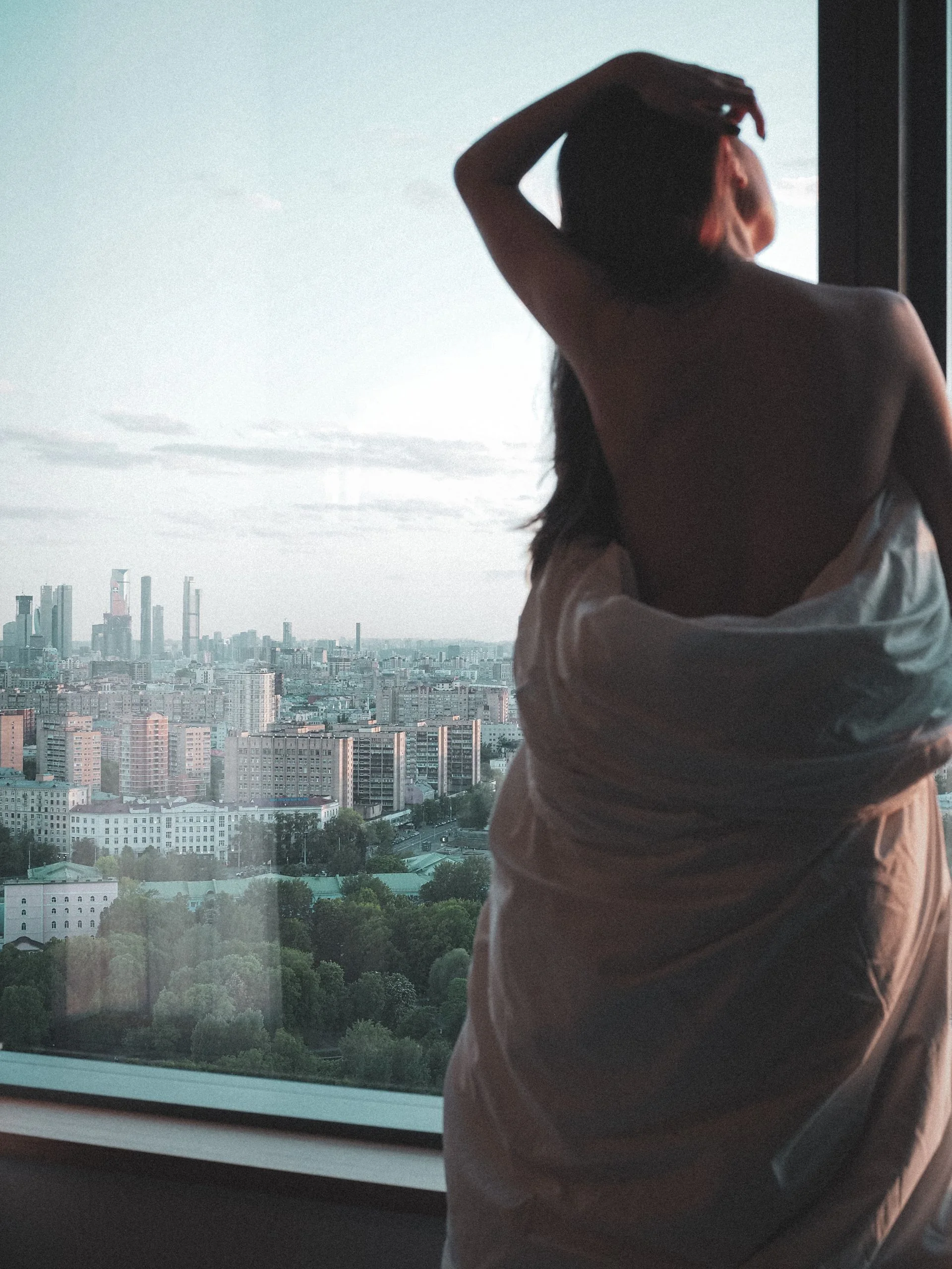 An adult wrapped in a blanket looking calmly out of a window
