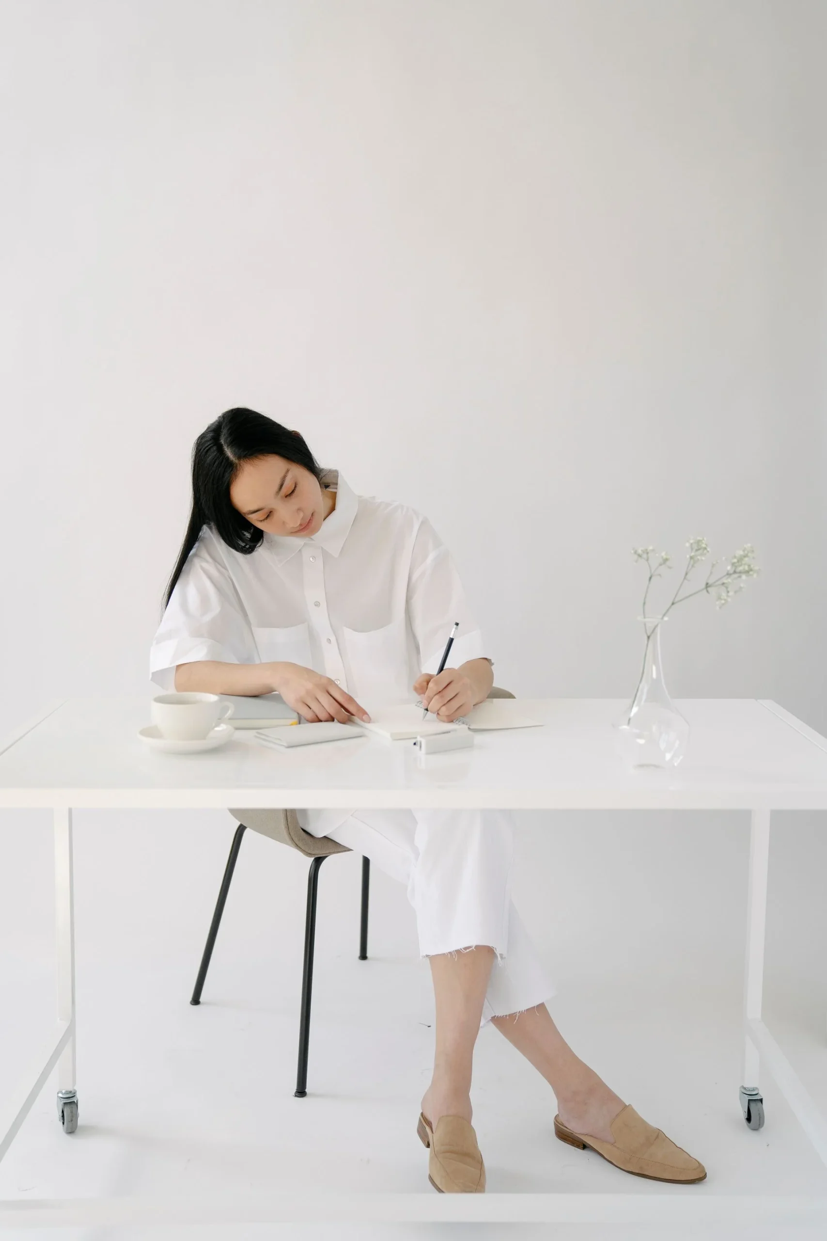 An adult writing in a notebook at a bright table